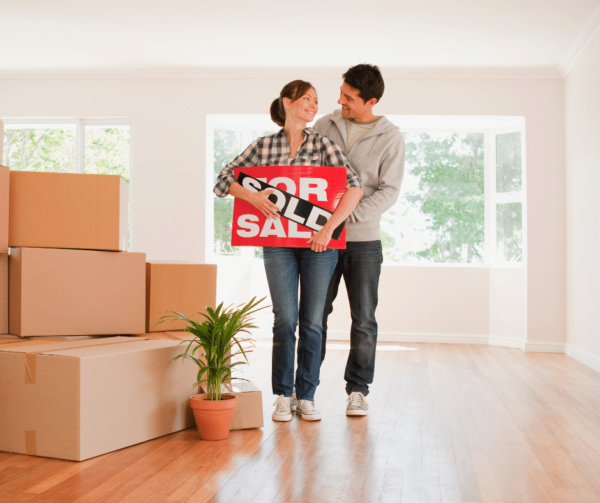 happy couple packing and holding sold house for cash sign